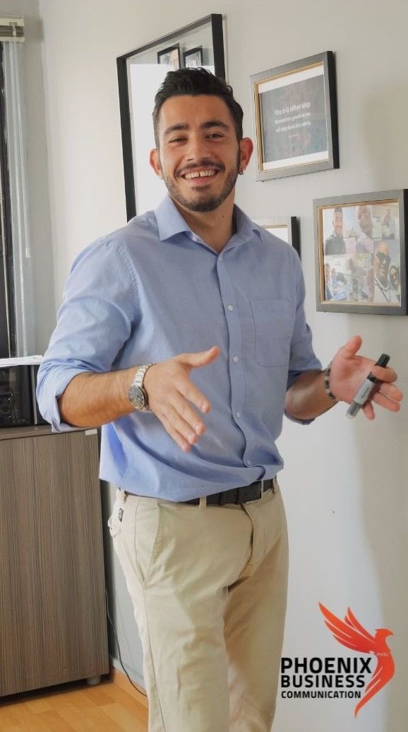 Man smiling and holding a marker while standing near framed photos on a wall.